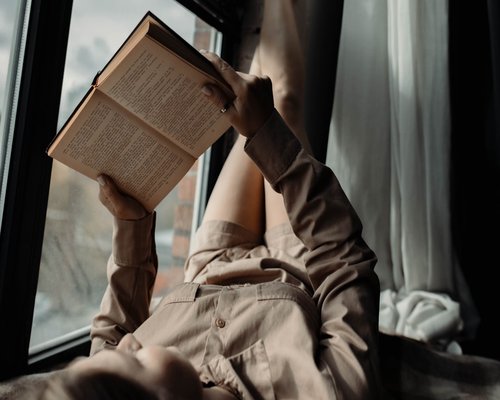 Person reading a book near a window with warm natural morning light